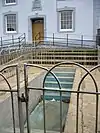 empty concrete baptismal pool with steps down into it and iron fence around