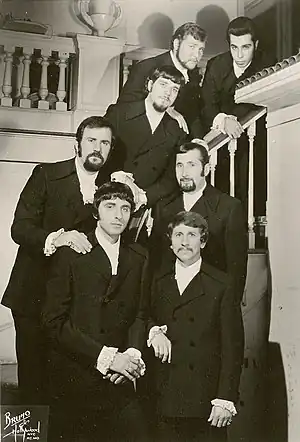 The band looking to the camera, standing on a stairwell, dressed in suits