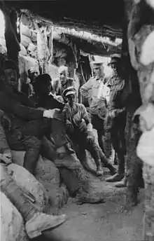 Soldiers sitting in a trench beneath a log roof