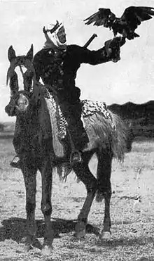 A black-and-white photograph of a mounted man on a dark horse. A hawk is perched on the man's outstretched hand.