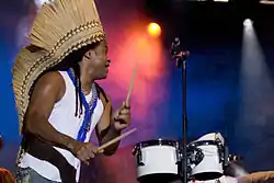 A side view of Carlinhos Brown performing drums.