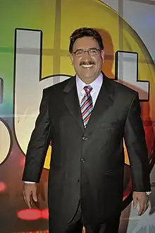 Smiling, middleaged, darkhaired mustachioed man, wearing glasses and a suit