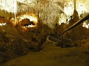 A picture of a partially illuminated cave with a jagged rock ceiling and a walkway extended into the cavern.