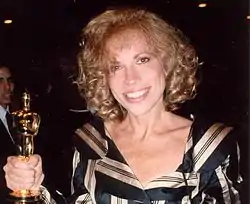 A blonde-haired woman in a black dress holding a gold statuette