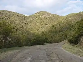 photo of a paved road, with crumbling pavement, and 3 hills in the distance