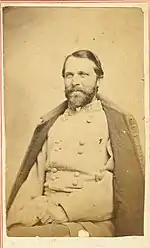 Sepia print of a seated, bearded man in a gray military uniform with a coat over his shoulders.