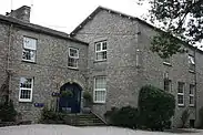 Large grey stone two-story building with a short staircase up to a blue entrance door,