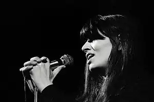 Black-and-white photograph of a woman with long dark hair holding a microphone and singing