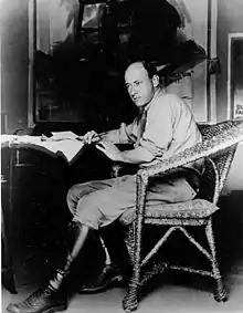 DeMille posing on a chair with a pen in hand