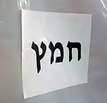 "Chametz" in large black Hebrew letters on a letter-size piece of paper, affixed horizontally to white plastic background.
