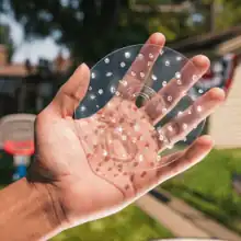 A photograph of a hand holding up a transparent CD covered with diamonds