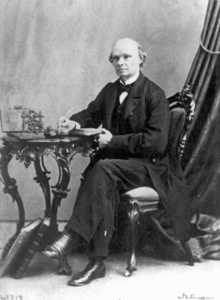 Photo fair-skinned man, balding, wearing a mid-Victorian business suit and seated at a table