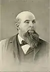 Mostly bald white male with a large goatee in a dark suit