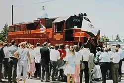 An audience in front of red CMNW diesel locomotive #2036 listens to Governor James R. Thompson