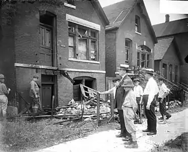 White men and boys standingin front of a vandalized house.