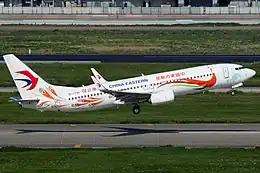 A white plane with peacock-themed livery seconds to touchdown