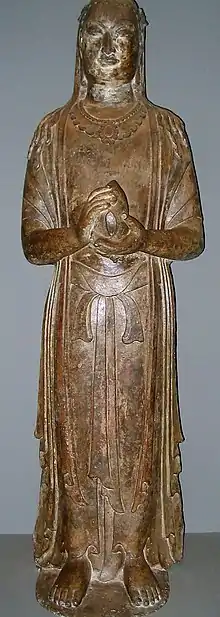 A standing Buddha: a yellow statue made from limestone, with its hands in prayer and holding a lotus