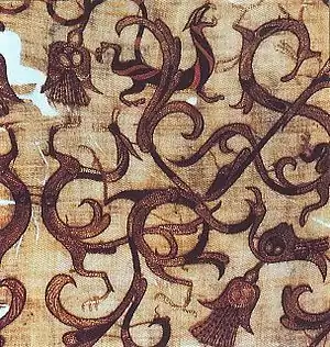 A fragile piece of silk, turned brown with age, showing an arabesque design of stylised dragons, phoenixes and tigers embroidered with chainstitching in dark red.
