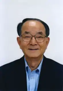 Head-and-shoulders portrait of the American entrepreneur, venture capitalist, and philanthropist Chong-Moon Lee. Lee, who emigrated from South Korea in 1970, is wearing wire-rimmed glasses a dark jacket with a blue-and-white striped collared shirt.