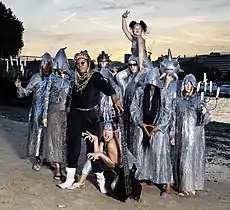 Chrome Hoof on a dawn/dusk Summer of 2007 river beach, dressed to promote 'Pre-Emptive False Rapture'.  Flanking members hold candelabra and most are wearing silvery cowls, with Shingai Shoniwa counterpointed in matt black.