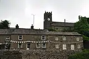 St Mary's Church behind houses on Main Street, was consecrated in 1580, but some components had been moved from earlier structures; the decorations in this image were added for the Tour de France (June 2014)