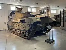 Tracked armoured vehicle with gun barrel and turret in situ inside a large museum gallery.