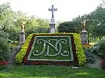 Floral display at the cemetery, with "NDC" on raised bed, cross and two statues of angels in the background