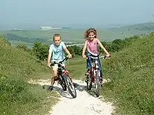 A boy and a girl riding bicycles on a trail through hills