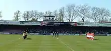 One of the stands of the Bootham Crescent association football ground, with supporters sitting down and players standing on a grass field below