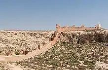 A line of square towers, connected by walls and topped with battlements (protective protrusions), spans the bottom to the top of a mountain slope.