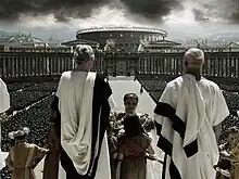 Men in white robes with the Colosseum in the background.