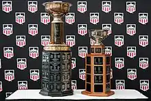 Two large trophies sitting on a table in front of a backdrop with multiple instances of the USHL logo