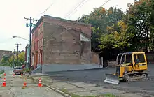 A large freshly paved lot with a yellow John Deere bulldozer sitting in the middle. In the rear are some of the buildings seen in the photo above, but not all of them