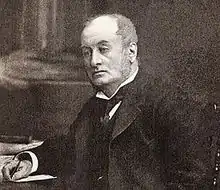  Head and upper body of a middle-aged man with receding hair, clean shaven, wearing a wing collar with tie, looking left. He is seated at a table, with a pen in his right hand.