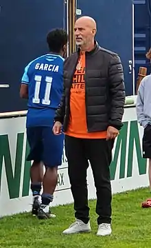 Stephen Hart standing up on the pitch wearing an orange "Every Child Matters" t-shirt.