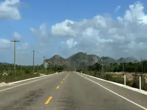 Picture of a two-lane road with broad shoulders, and hills in the background.