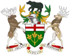 A central shield with the upper part showing the red cross of St. George and the lower part showing three golden maple leaves on a green background. There is a black bear on top of a knight's helmet above the shield with a moose to the left and a Canadian deer to the right. The province's motto "Ut incepit Fidelis sic permanent", Latin for "Loyal she began, loyal she remains" is written below the crest.