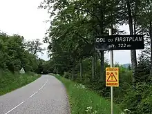 Tree-lined summit of a road with a sign post reading "Col du Firstplan, alt. 722m"