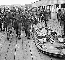 Commandos marching away from a quayside. A collapsible Goatley boat is to their right.