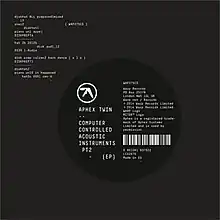 A grey background featuring white monospace text in the upper-left corner and a black circle slightly off centre to the right. Inside the circle a white logo is visible and "Aphex Twin - - Computer Controlled Acoustic Instruments pt2" is written in a block white monospace typeface; to the right of the white text, a barcode is visible as well as other miscellaneous text.