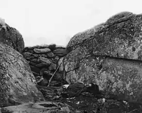 Post-battle Confederate sharpshooter body staged behind the "Devil's Den barricade" illustrating "a sharpshooter…of Devil's Den" such as the one presumed killed by a percussion of a cannon shot from Little Round Top after Weed and Hazlett had been sniped. Tenatively identified 2018 as a Georgia soldier.