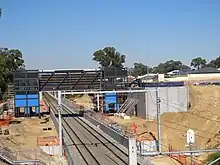 View from a bridge of a dual-tracked railway line with concrete retaining walls and a metal concourse under construction