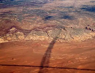 Shadows of contrails over San Rafael Reef —San Rafael Swell, Reef (perimeter), and San Rafael Desert at south & southeast. The Reef is most of the southeast, and east perimeter of the 45-mile-wide (72 km) (west-to-east) San Rafael Swell, which trends southwest-by-northeast.