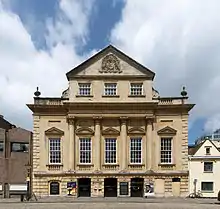An imposing eighteenth-century building with three entrance archways, large first-floor windows and an ornate peaked gable end above.
