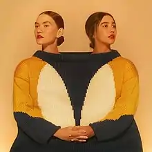 Ana and Vitória side by side inside the same sweater, looking towards slightly opposite directions and holding hands