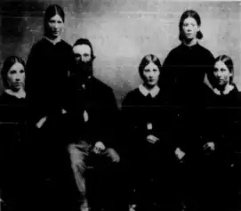 black-and-white photo of a husband and wife and their four daughters, all dressed in dark-colored dresses
