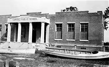 boats tied to the porch of a brick school house after a hurricane