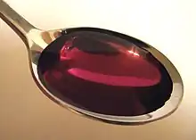 Close-up photo of a metal spoon filled with a viscous, clear purple fluid