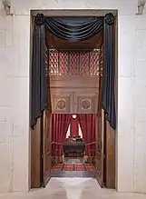 The courtroom doors of the Supreme Court draped in black. Through the open doors is visible Ginsburg's seat and the bench before the seat, each also draped in black.
