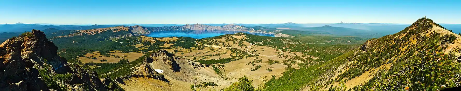 A panorama shot displays Crater Lake in the center background, with mountains in the foreground on the left and right